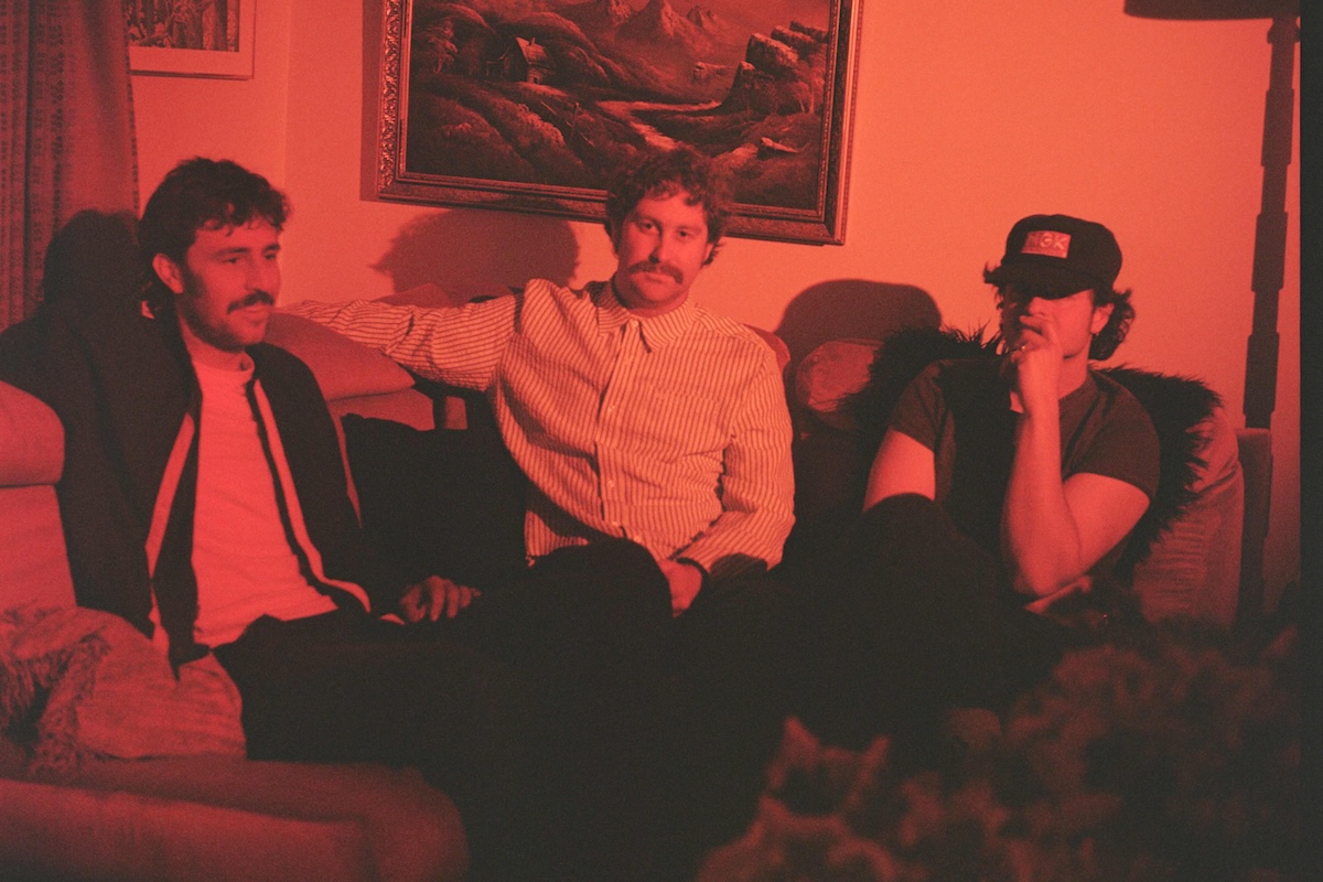 Australian garage rock trio The Grogans sitting together on a couch under warm red lighting in a room.